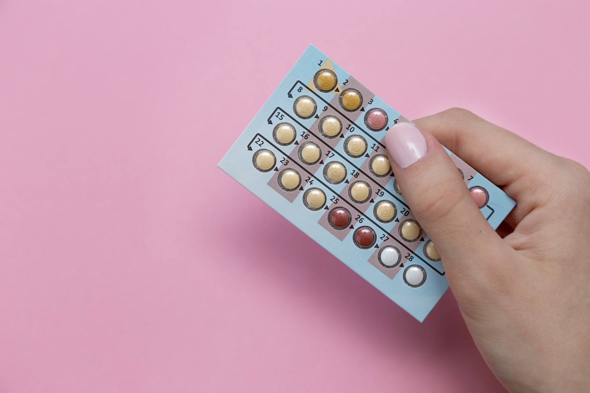 Blister of oral contraceptives in a female hand on a pink background with free space for text