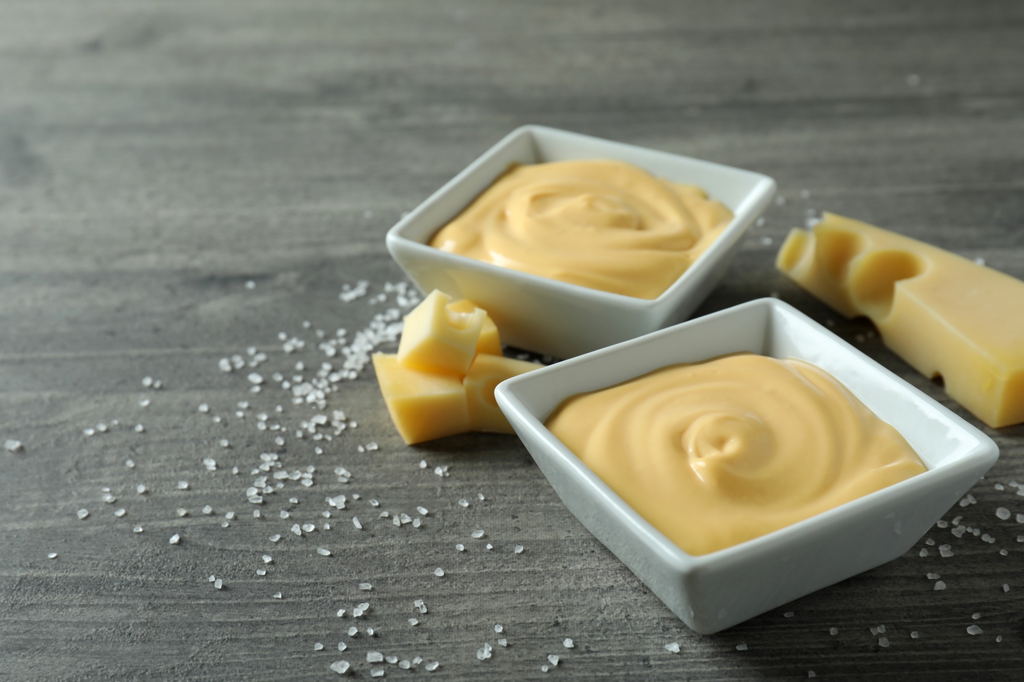 Bowls with cheese sauce, cheese and salt on gray textured table