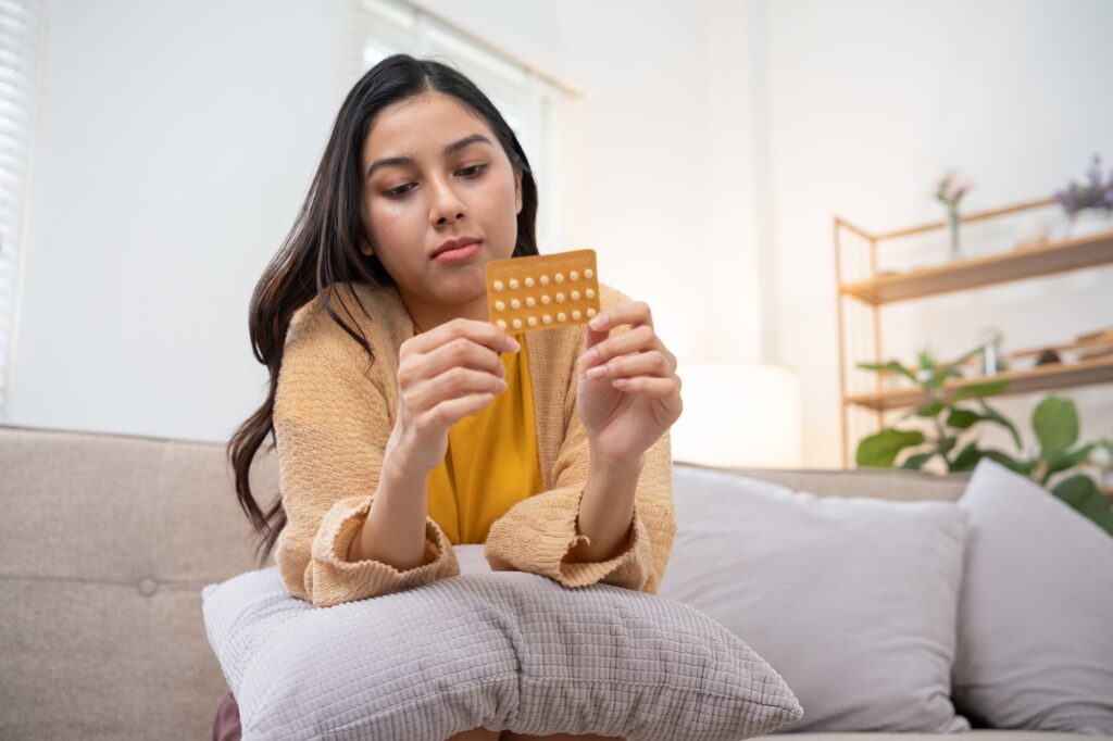 Young Woman Holding Birth Control Pills While Sitting on Couch in Modern Living Room
